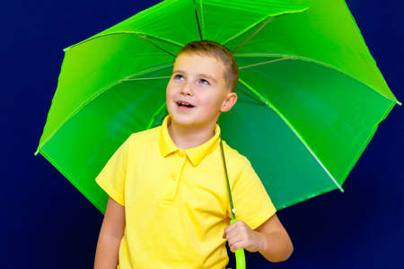 Attractive playful caucasian blond schoolboy with umbrella on blue studio background.Boy shows all kinds of grimaces.close up imageの写真素材