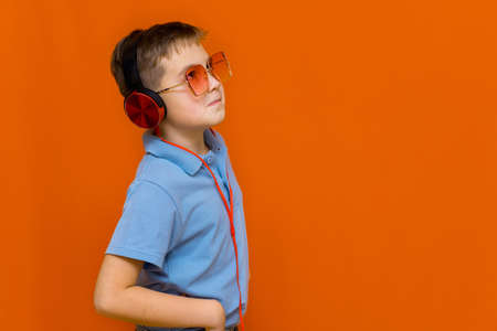 attracive young kid wearing red glasses is listening music with red headphones on orange studio backgroundの写真素材