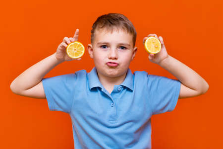 Close up Caucasian young child shows raw slices of lemon on a orange background. Healthy, lifestyle and a happy childhood concept.の写真素材
