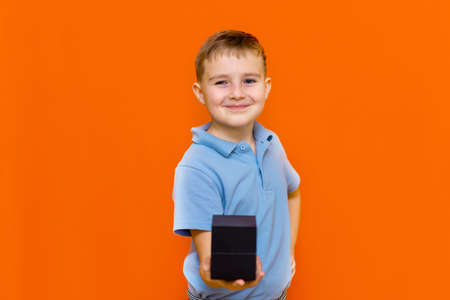 Little boy in t shirt holding black present for girl or mother, Valentines day, mother's day, orange studio wall.の写真素材