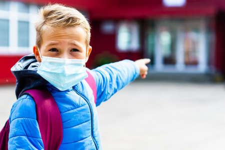 Close up image Attractive schoolboy in protective mask standing outdoor excited child points finger at school Back to school. epidemic influenza and coronavirusesの写真素材