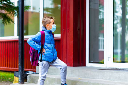 Side view Schoolboy wearing protective mask casual clothes and carry a backpack standing near school. Child going school after pandemic over. students are ready for second pandemic waveの写真素材