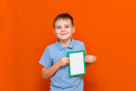 Portrait of caucasian schoolboy in t-shirt posing isolated on orange background. Mock up copy space. Shows to the white empty blank billboard with place for text or image.の写真素材
