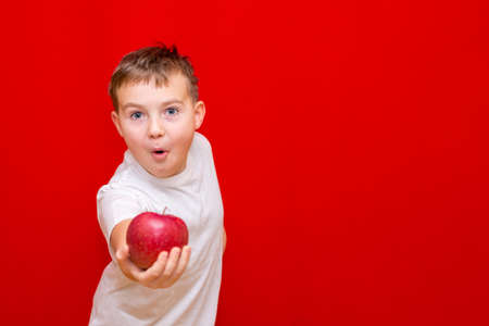Close up European boy kid child schoolboy apple gives in front.Vitamins and fruits, healthy food. Prtrait of a happy beautiful child on a bright red background.の写真素材