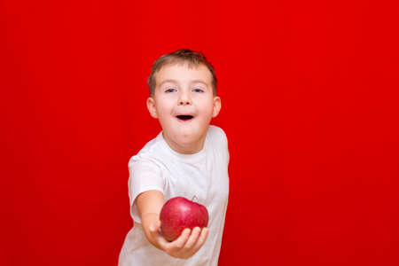 Close up European boy kid child schoolboy apple gives in front.Vitamins and fruits, healthy food. Prtrait of a happy beautiful child on a bright red background.の写真素材