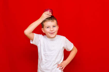 Close up European boy kid child schoolboy holds a red Apple oin his hands. Vitamins and fruits, healthy food. Prtrait of a happy beautiful child on a bright red background.の写真素材