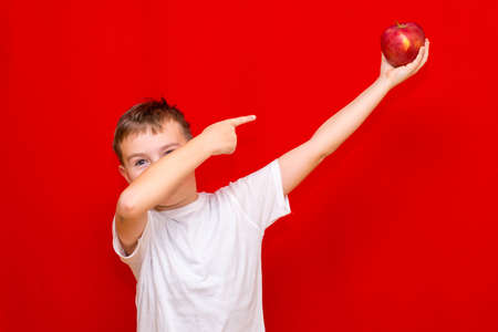 Close up European boy kid child schoolboy holds a red Apple oin his hands. Vitamins and fruits, healthy food. Prtrait of a happy beautiful child on a bright red background.の写真素材