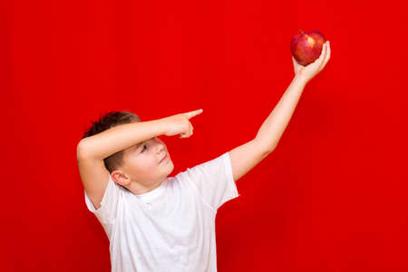 Side view Close up European smiling boy kid child schoolboy holds a red Apple oin his hands. Vitamins and fruits, healthy food. Prtrait of a happy beautiful child on a bright red background.の写真素材