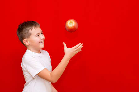 Side view Close up European boy kid child schoolboy throw up apple Prtrait of a happy beautiful child on a bright red background.の写真素材