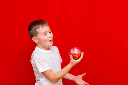 Side view Close up European boy kid child schoolboy throw up apple Prtrait of a happy beautiful child on a bright red background.の写真素材