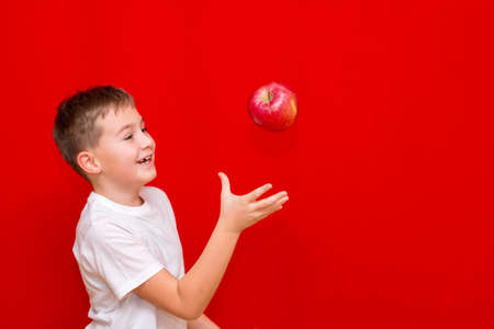 Side view Close up European boy kid child schoolboy throw up apple Prtrait of a happy beautiful child on a bright red background.の写真素材