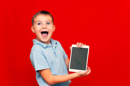 Laughing Child with a tablet pc. Boy shows empty tablet on red backgroundの写真素材
