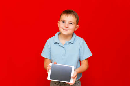 Child with a tablet pc. Boy is some thinking and shows empty tablet on red backgroundの写真素材