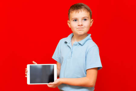 Child with a tablet pc. Boy is some thinking and shows empty tablet on red backgroundの写真素材