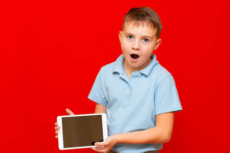 Surprised Child with a tablet pc. Boy shows empty tablet on red backgroundの写真素材