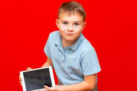 schoolboy leaned forward and shows empty tablet on red background advertisement mock up bannerの写真素材