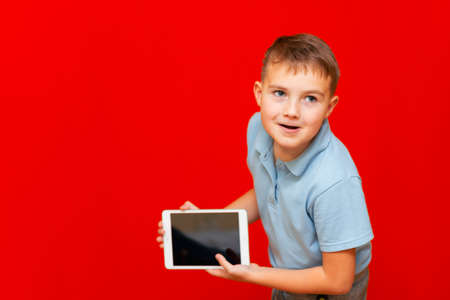 schoolboy leaned forward and shows empty tablet on red background advertisement mock up bannerの写真素材