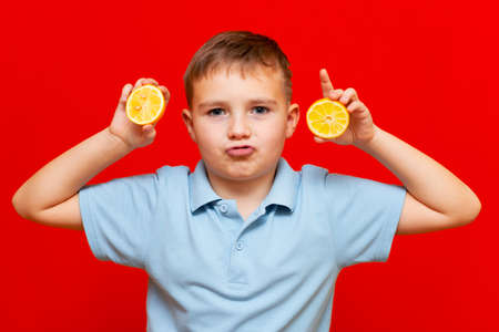 Healthy lifestyle people. Funny image of confident school boy showing two lemons. Isolated on trendy red backgroundの写真素材