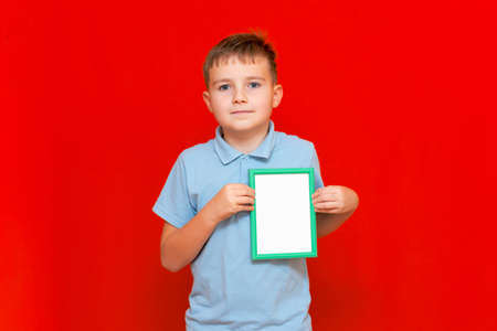 Happy small 9s boy holding a blank board advertisement mock up on red trendy bright background.の写真素材