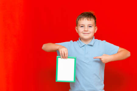 lovely small 9s boy showing a blank board advertisement mock up with his finger on red trendy bright background.の写真素材
