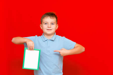 lovely small 9s boy showing a blank board advertisement mock up with his finger on red trendy bright background.の写真素材