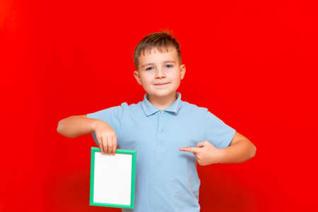lovely small 9s boy showing a blank board advertisement mock up with his finger on red trendy bright background.の写真素材