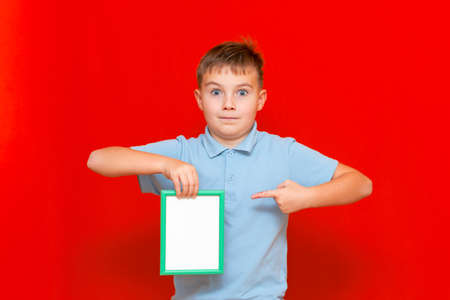 lovely small 9s boy showing a blank board advertisement mock up with his finger on red trendy bright background.の写真素材