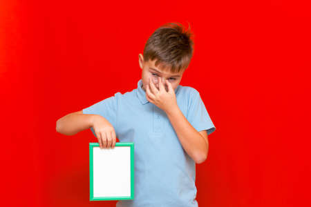 Upset small 9s boy holding a blank board advertisement mock up on red trendy bright background.の写真素材