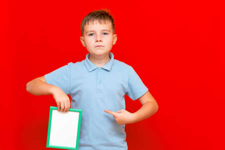 lovely small 9s boy showing a blank board advertisement mock up with his finger on red trendy bright background.の写真素材