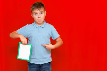 surprised small 9s boy shows a blank board advertisement mock up on red trendy bright background.の写真素材