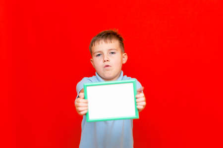 Happy small 9s boy holding in front a blank board advertisement mock up on red trendy bright background.の写真素材