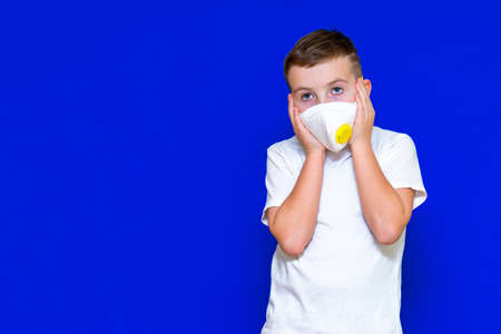 Close up Portrait of caucasian boy in a protective mask respirator his hands to a head blue bright background.の写真素材