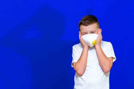 Close up Portrait of caucasian boy in a protective mask respirator his hands to a head blue bright background.の写真素材