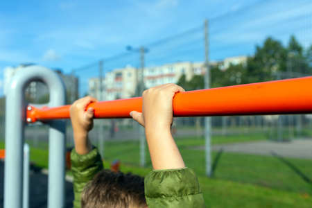 Close up Boy hands kid child 9s in casual clothes performing pull-ups outdoor exercise machines
