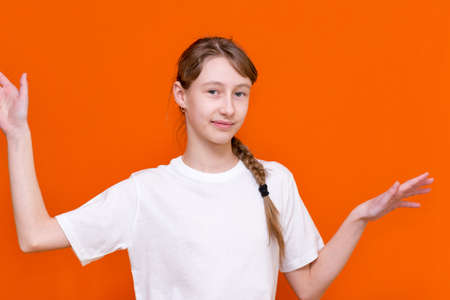 Close up portrait of happy youn child girl spreading hands aside, wearing casual white t-shirt, posing against orange wall looks at camera, expressing positive emotions.の写真素材