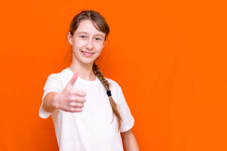 Close up A caucasian smiling little long haired one braid girl in blank white t-shirt showing thumbs...