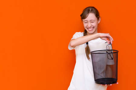 Close up smiling calm serious young girl throw away her glasses in the trash binの写真素材