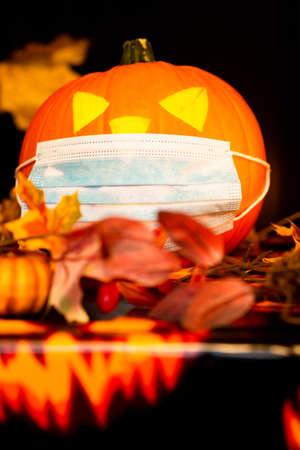 Close up Jack o lantern pumpkin on adark yellow maple leaves background with medical face mask.の写真素材