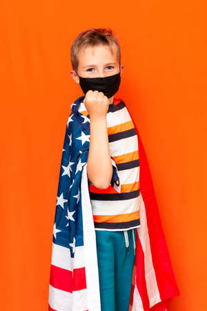 Calm boy wearing black face mask as a boxer on the shoulder usa flag on a orange backgroundの写真素材