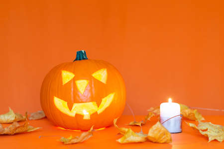 Glowing Halloween pumpkin head jack lantern burning candle on trendy orange table background copy space banner advertisementの写真素材