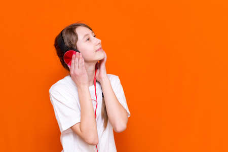 Attractive 12s girl in white t-shirt listens to music on red headphones closeup in a studio indoorの写真素材