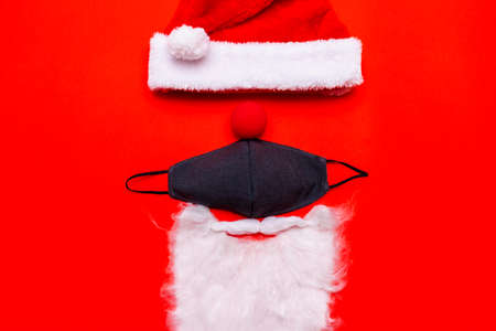 Coronavirus Christmas. Santa Claus Hat red nose black face mask white beard.Flat lay top view red...