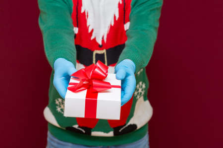Close up cropped shot of male hands holding white gift box on red studio background.Christmas concept.の写真素材