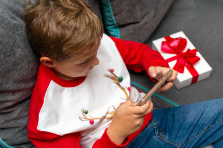 Top view Attractive kid boy using smartphone on Christmas holidays white gift for xmas photo at homeの写真素材