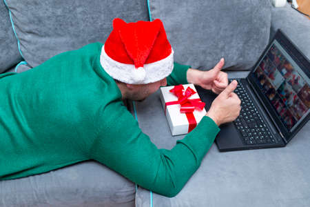 Side view Male man virtually exchanging Christmas gifts shows thumb up and having video call over a laptop at home on the couch.の写真素材