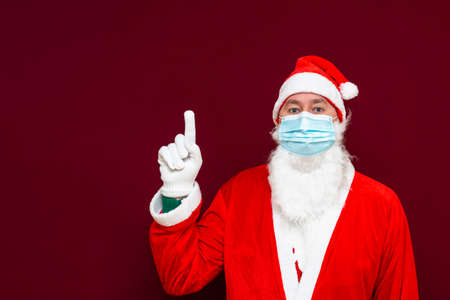 Side view Santa Claus man wears face mask shows to copy space safe from coronavirus covid-19 during quarantine on red studio background.Close up.の写真素材