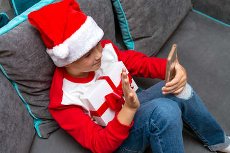Handsome kid boy in Santa Claus hat looks at smartphone screen, Talk with family,closeup image.の写真素材