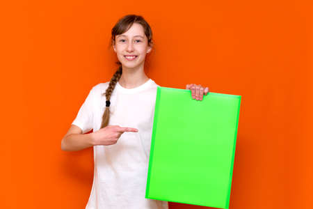 Surprised young girl poke at folder with a banner advertisement on a orange studio background. copy space bannerの写真素材