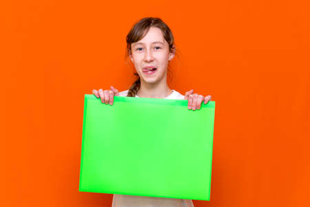 Mysterious young girl hiding under folder with a banner advertisement on a orange studio background. advertising copy spaceの写真素材