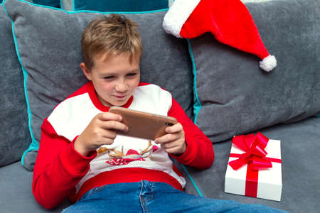 Front view Attractive kid boy using smartphone on Christmas holidays white gift for xmas photo at homeの写真素材